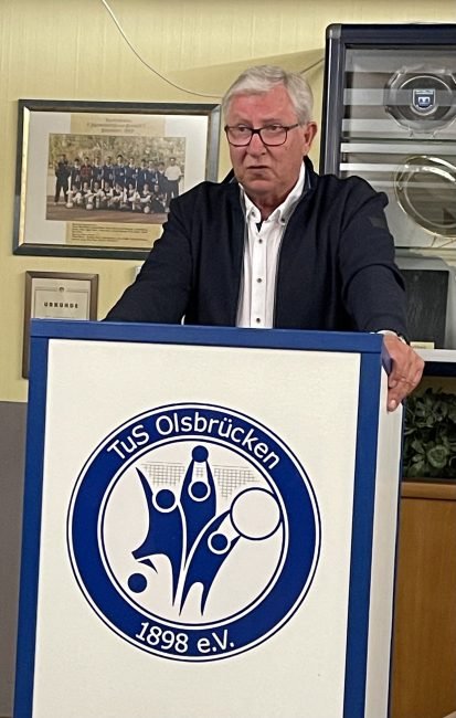 Dieter Gehrke steht am Rednerpult auf dem sich das Logo des TuS Olsbrücken befindet.